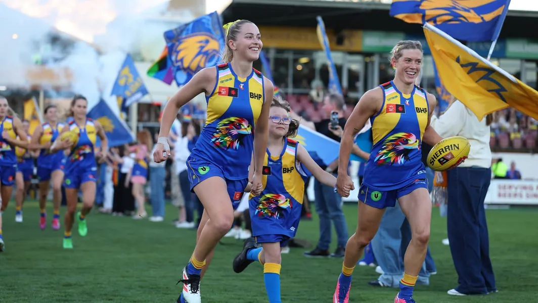 West Coast Eagles players and a young mascot in pride-themed jerseys